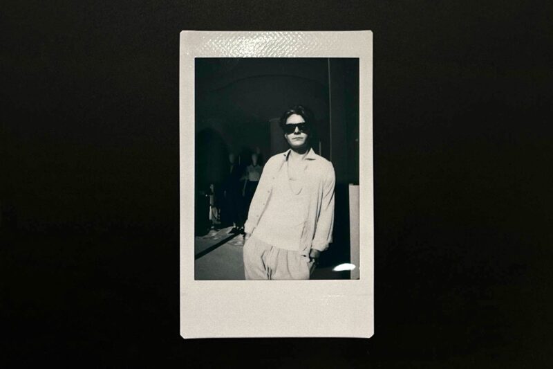 A Black and white picture of a man with white shirt and sunglasses in a black background