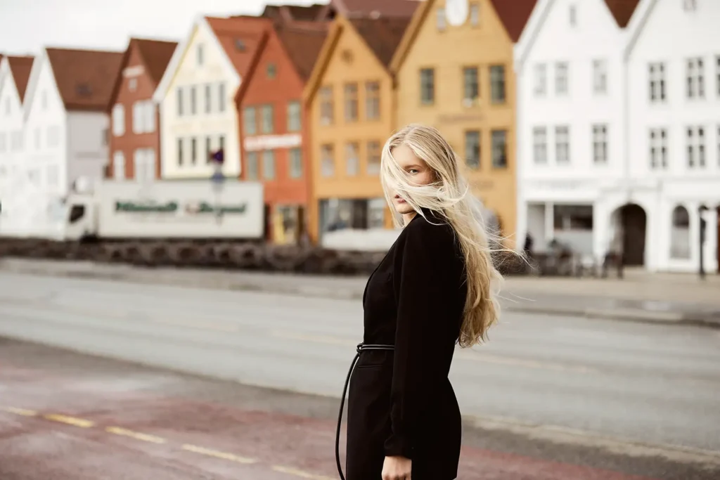 A female model with blonde hair wearing a black outfit posing to Ed Mehravaran Camera in Bergen in front of the famous colorful houses in Bergen.