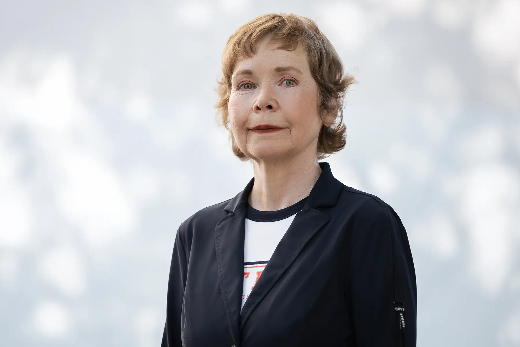 Portrait of Caroline Siege with short, wavy reddish hair and green eyes. Wearing a black blazer over a white t-shirt. She photographed outdoors in Berlin, Lichtenberg, against a soft background.
