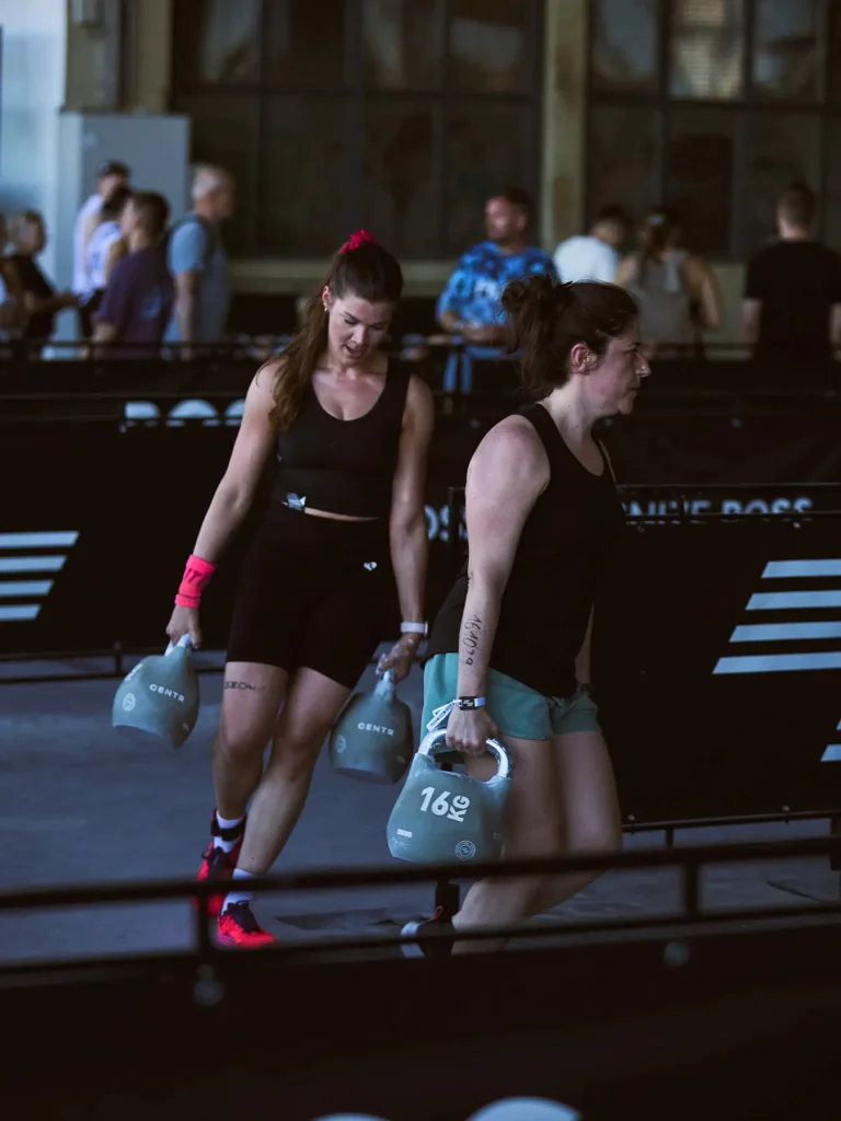 Magdaa in Farmer’s carry station in HYROX Berlin. Is carrying 16 kilograms weights in each of her hands and in front of her there is another female athletes