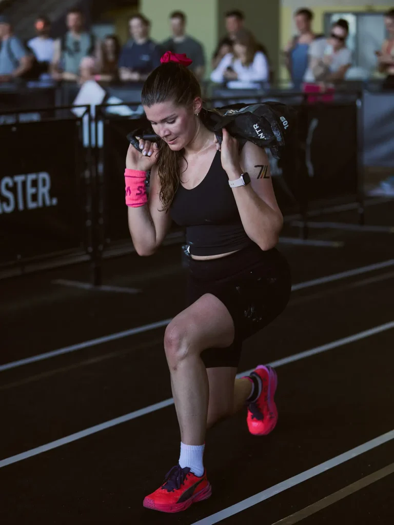 This is sandbag lunge station in HYROX race. Magda careing a 10 kg sandbag lunge on her shoulders at HYROX Berlin