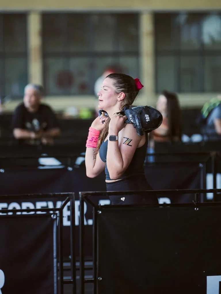 This is sandbag lunge station in HYROX race. Magda careing a 10 kg sandbag lunge on her shoulders at HYROX Berlin. She's looking so tired and exhausted