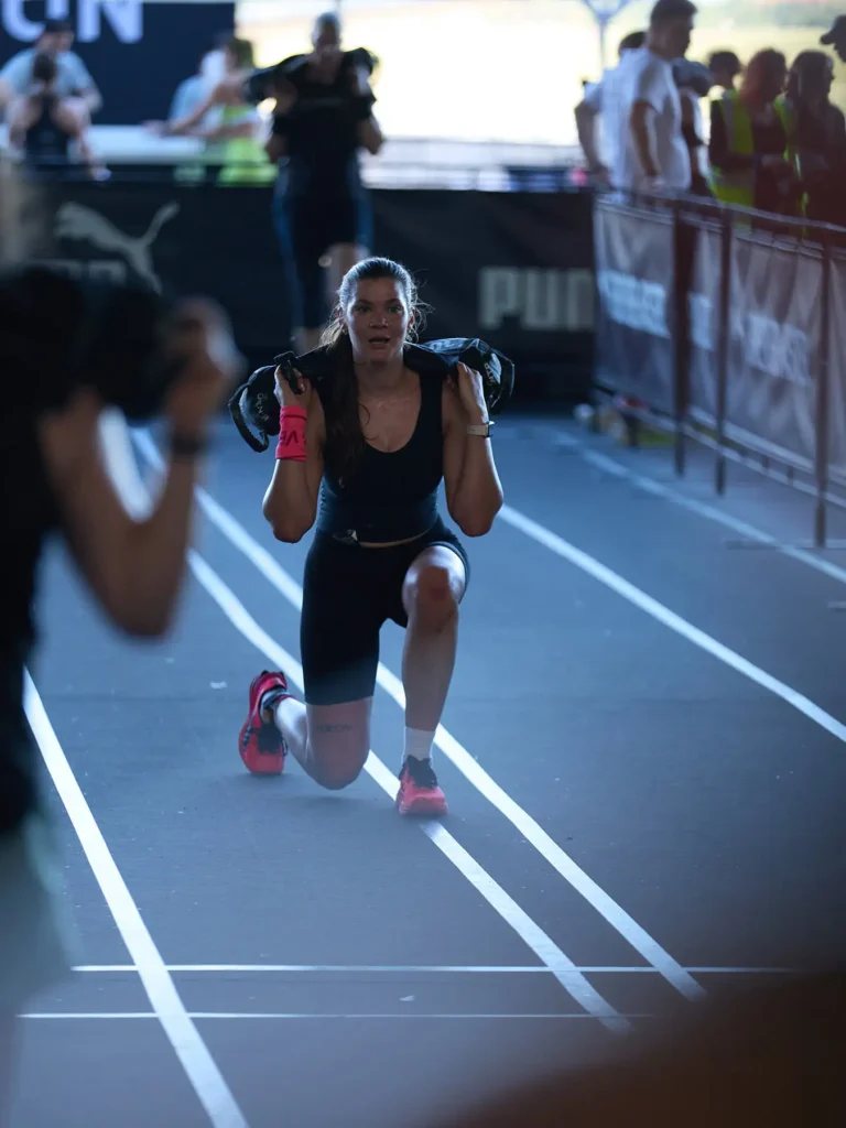 This is sandbag lunge station in HYROX race. Magda careing a 10 kg sandbag lunge on her shoulders at HYROX Berlin.