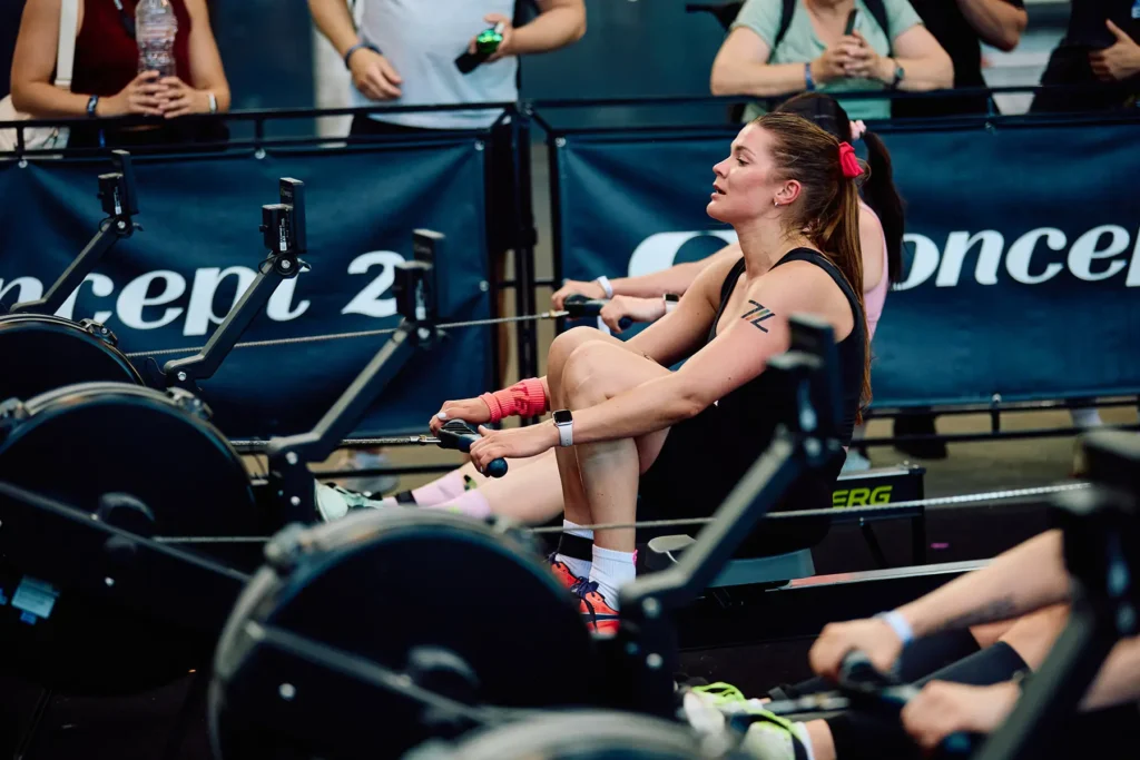 Magda rowing on a Concept2 machine at HYROX Berlin 2026, with other competitors alongside her and spectators behind the barrier.